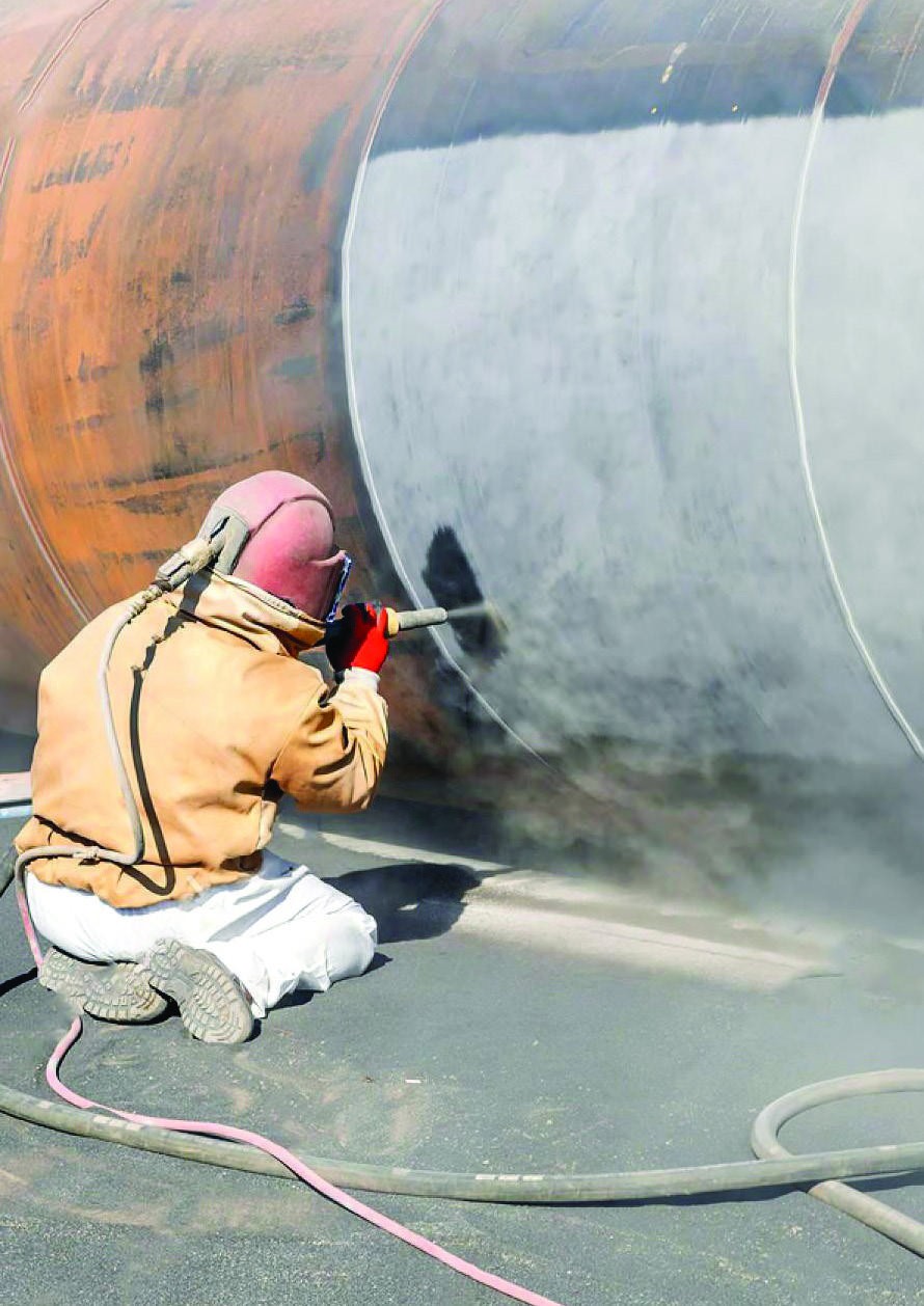 Worker sandblasting a large metal structure